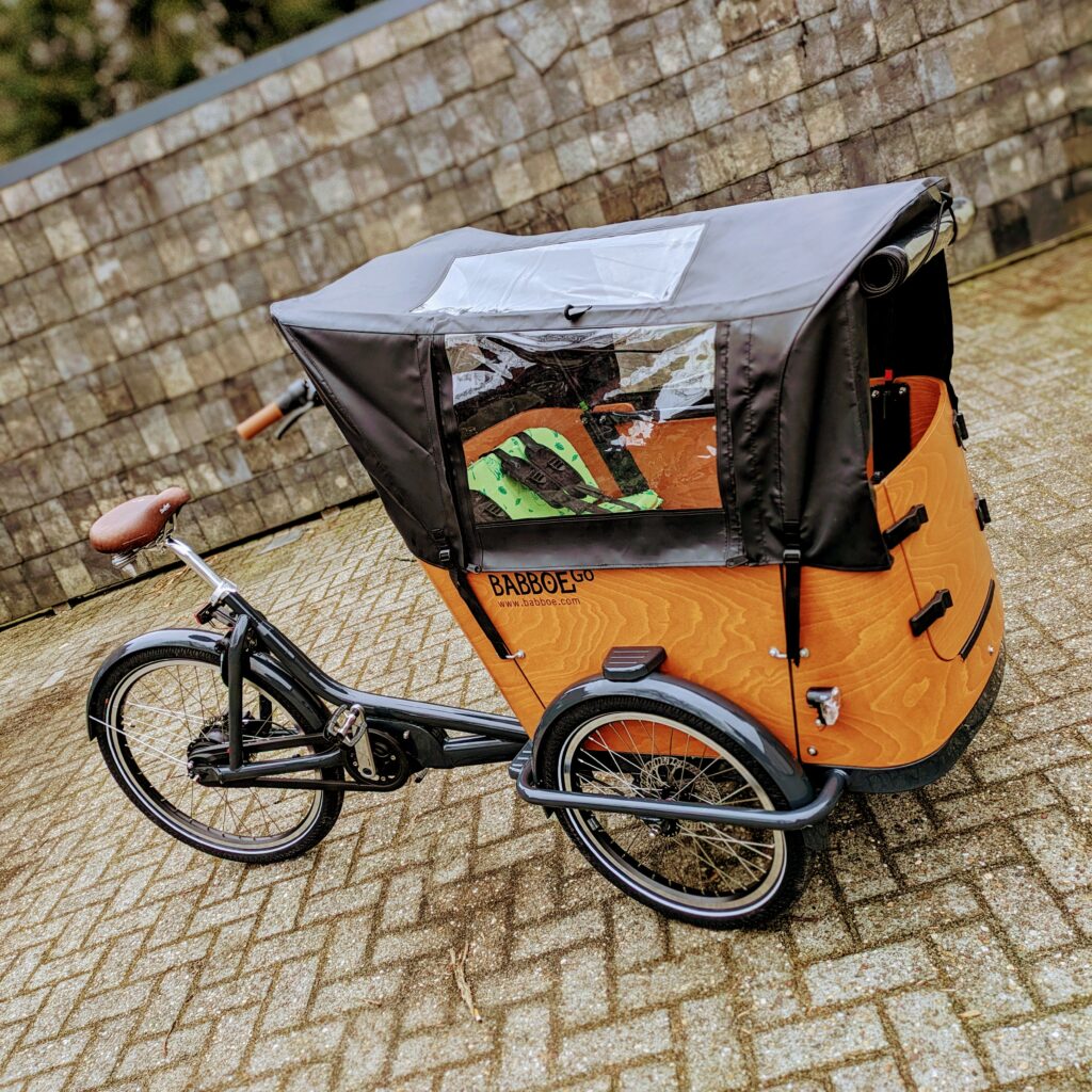 Babboe Go M cargo e-bike with wooden cargo/passenger box and black rain tent
