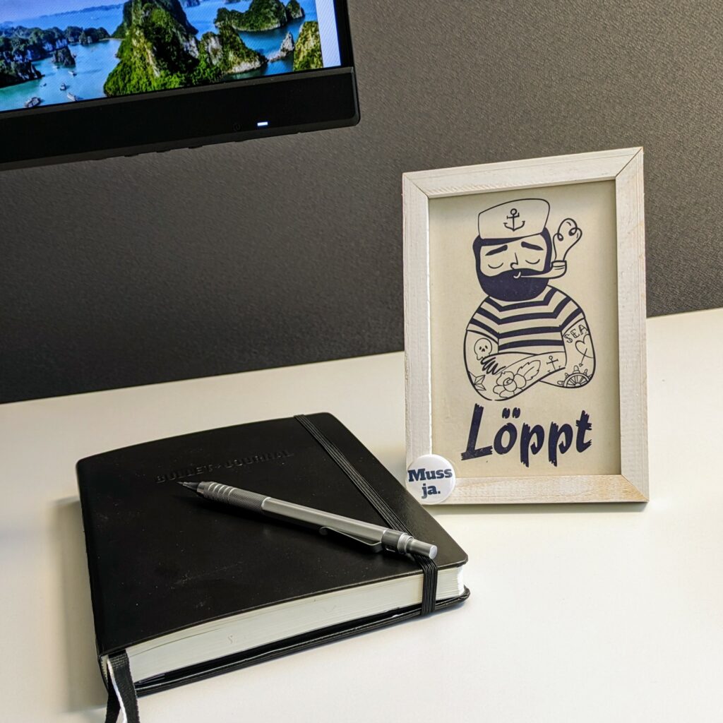 Illustration of a sailor, pipe, anchor tattoo on the arm and all, facial expression quite chill. Caption saying: “löppt”, northern German slang for “läuft”, which would translate into “its going well”. Attached to the bottom left is a round pin saying “muss ja”, which is such an innately German expression, it doesn't translate at all.