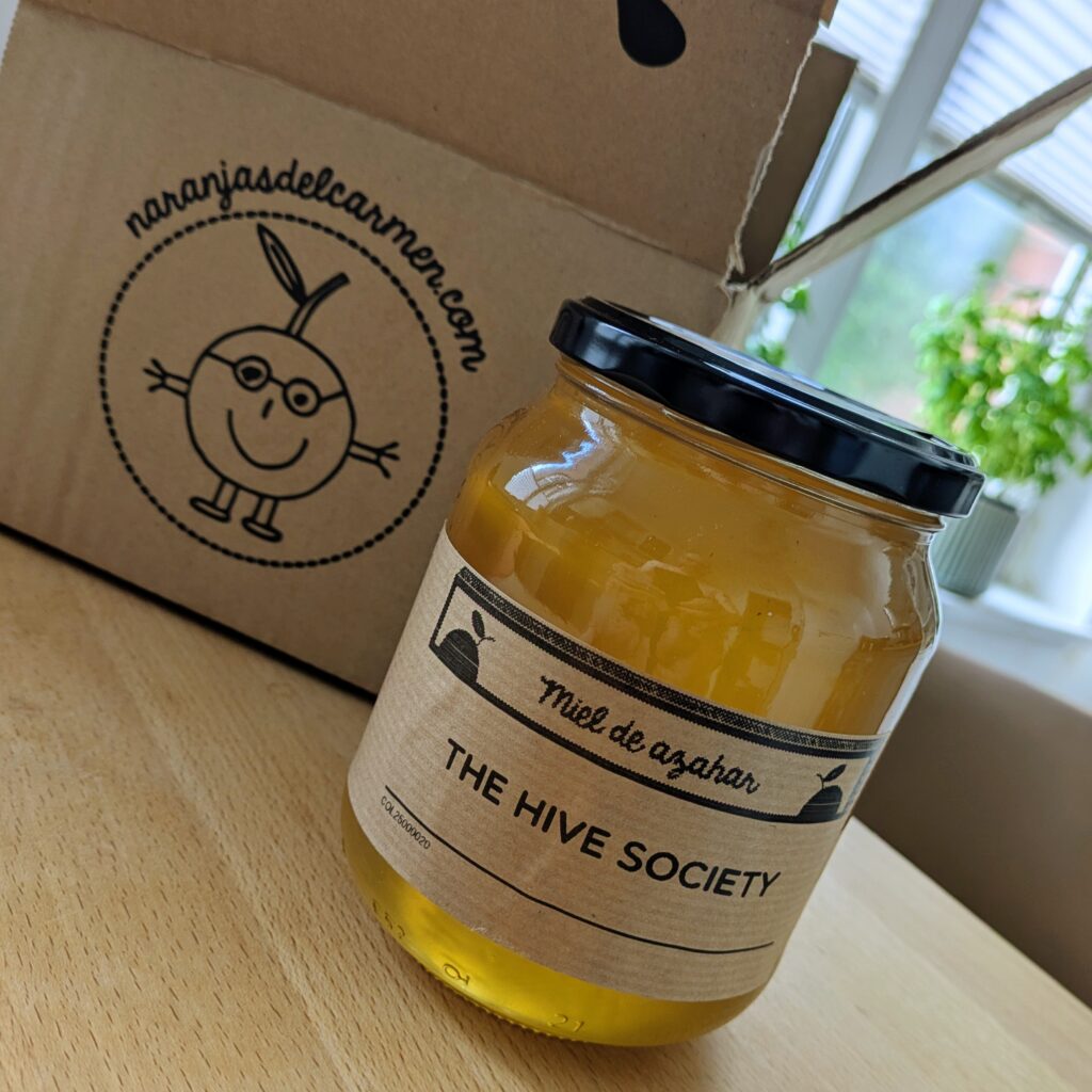 Big jar of honey with a beige paper label captioned The Hive Society